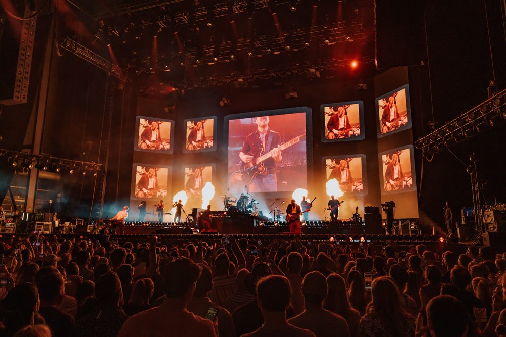 A Mumford and Sons LED wall filling the stage, the band small beneath it and the house full