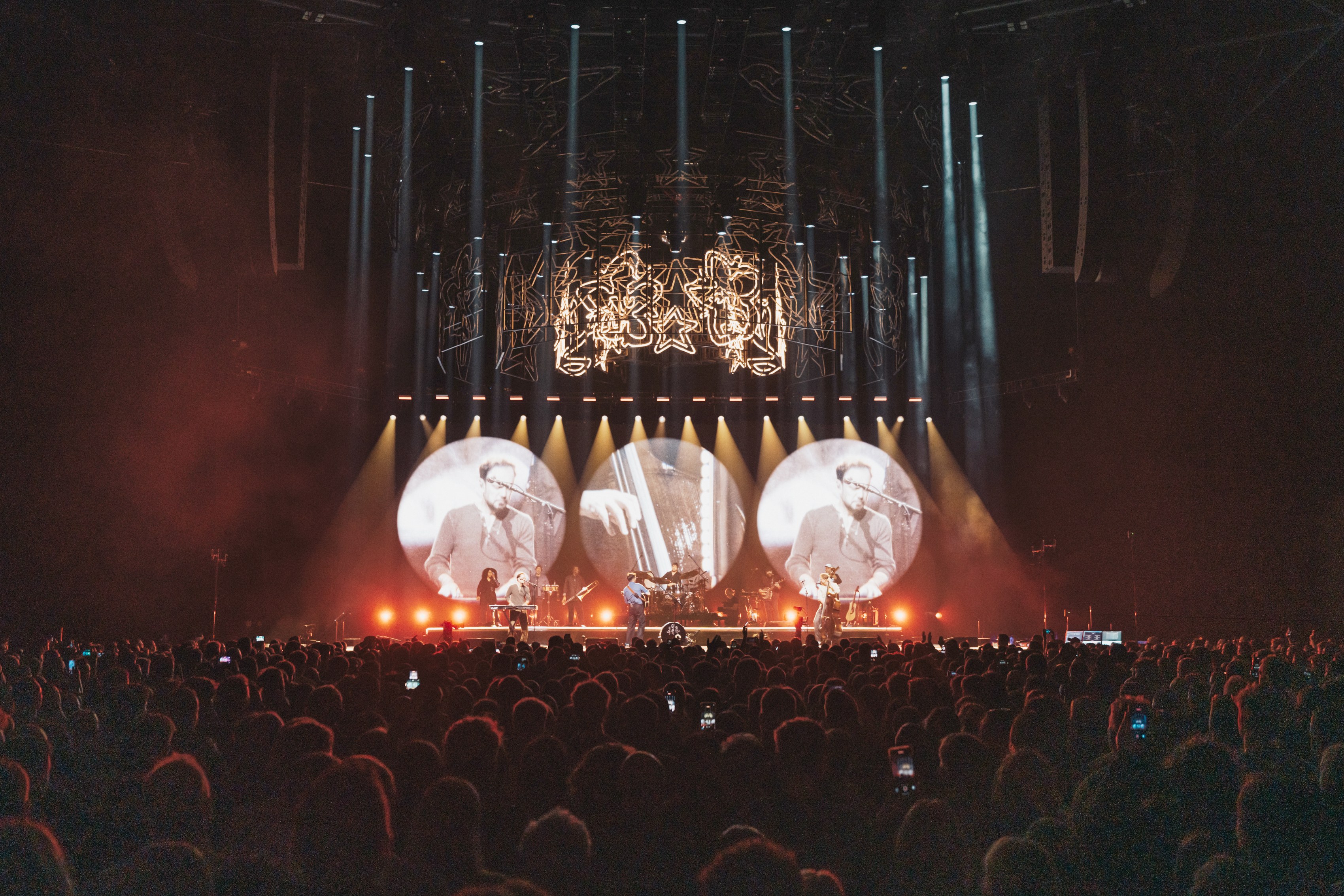 Three circular screens above a stage, each carrying the same face, lit in red from below
